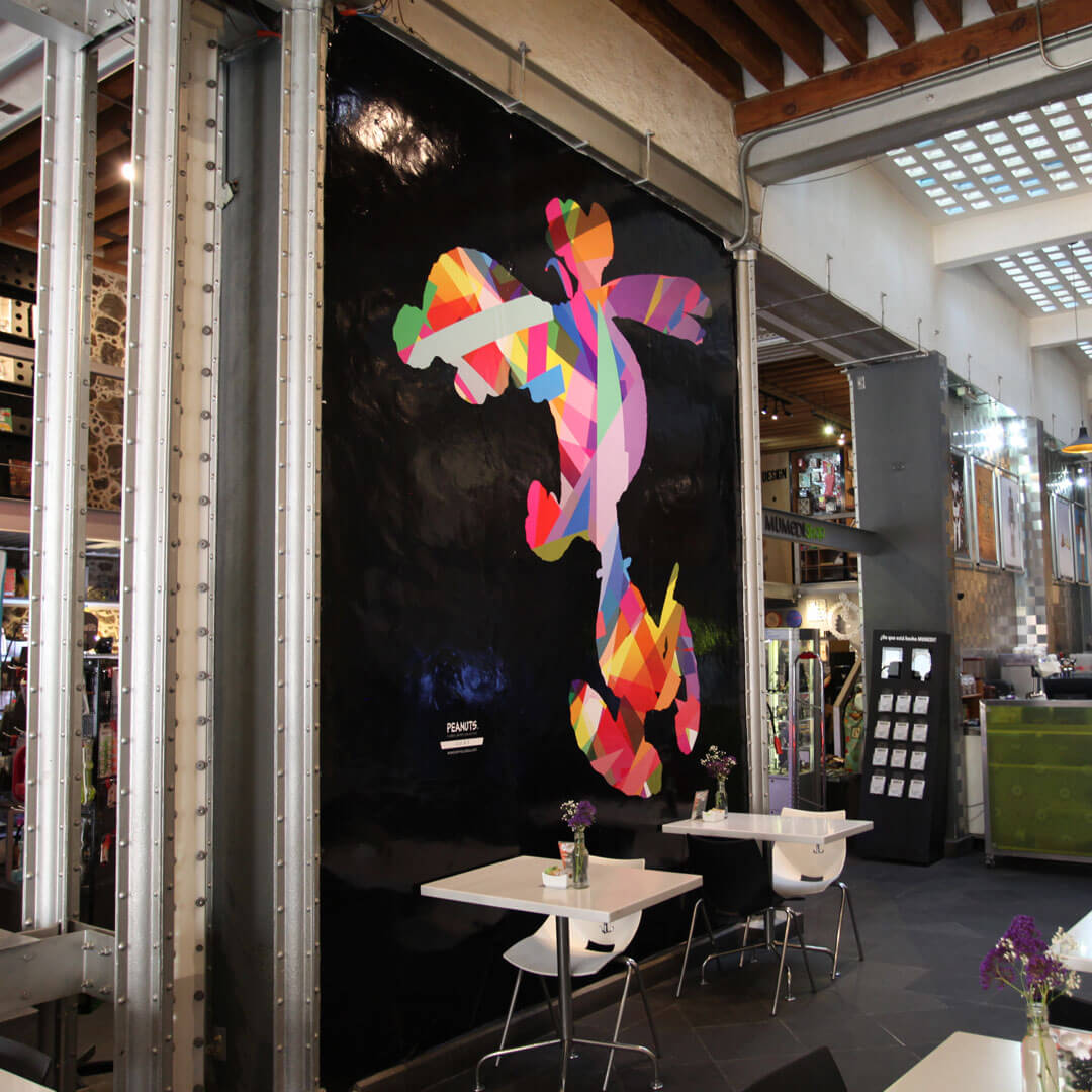 A café with white tables and a large colourful mural of a dog on a black wall.