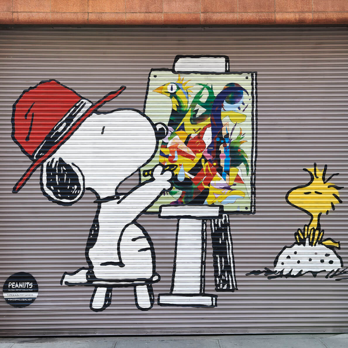 A mural on a garage door of a white dog sitting on a chair and painting a little yellow bird sitting in front of him.