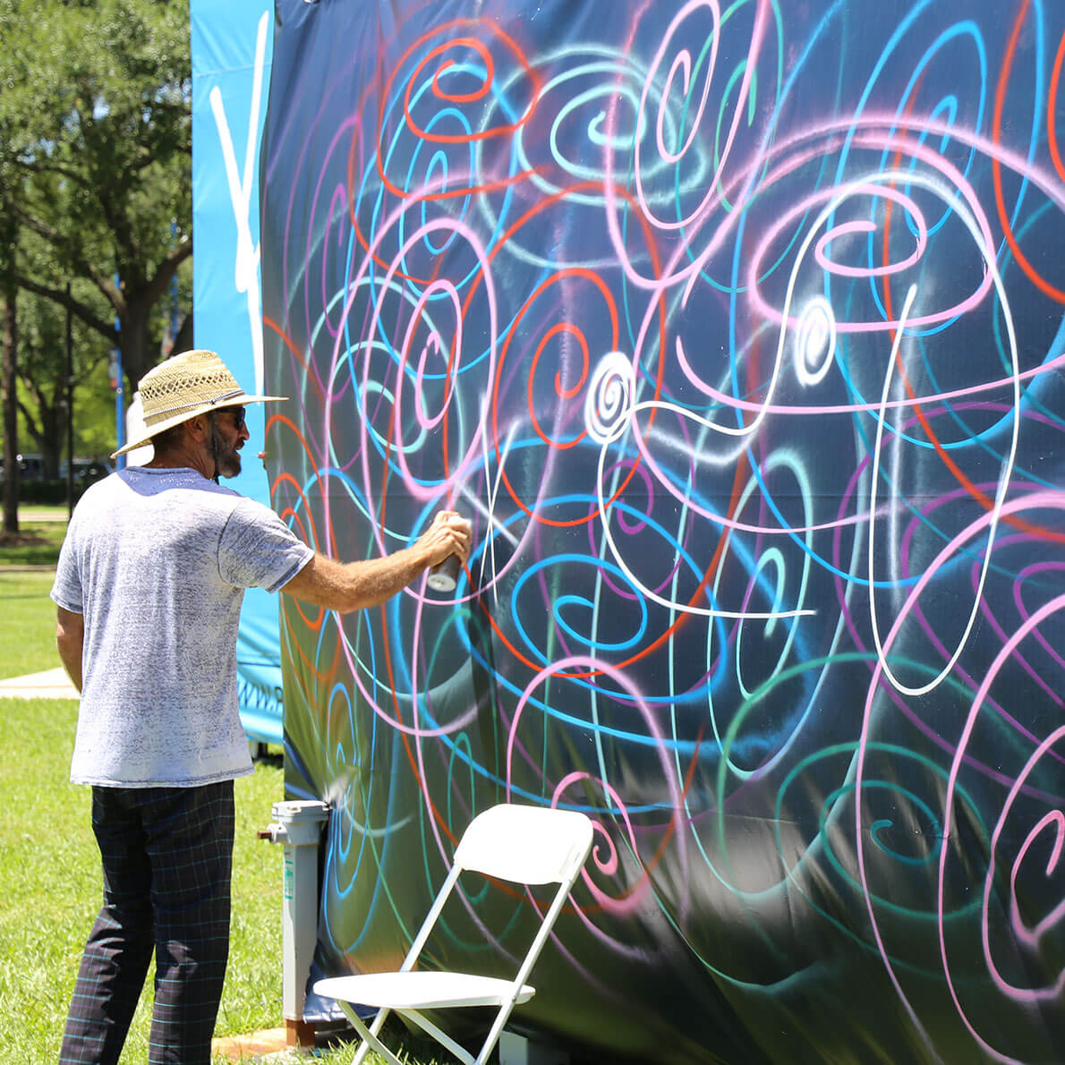 A man spray painting on a large piece of fabric in a park.