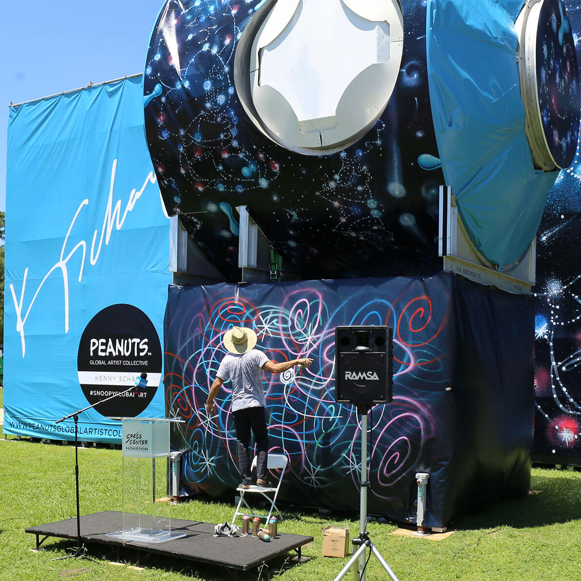 A man standing on a chair and spray painting three large structures in a park.