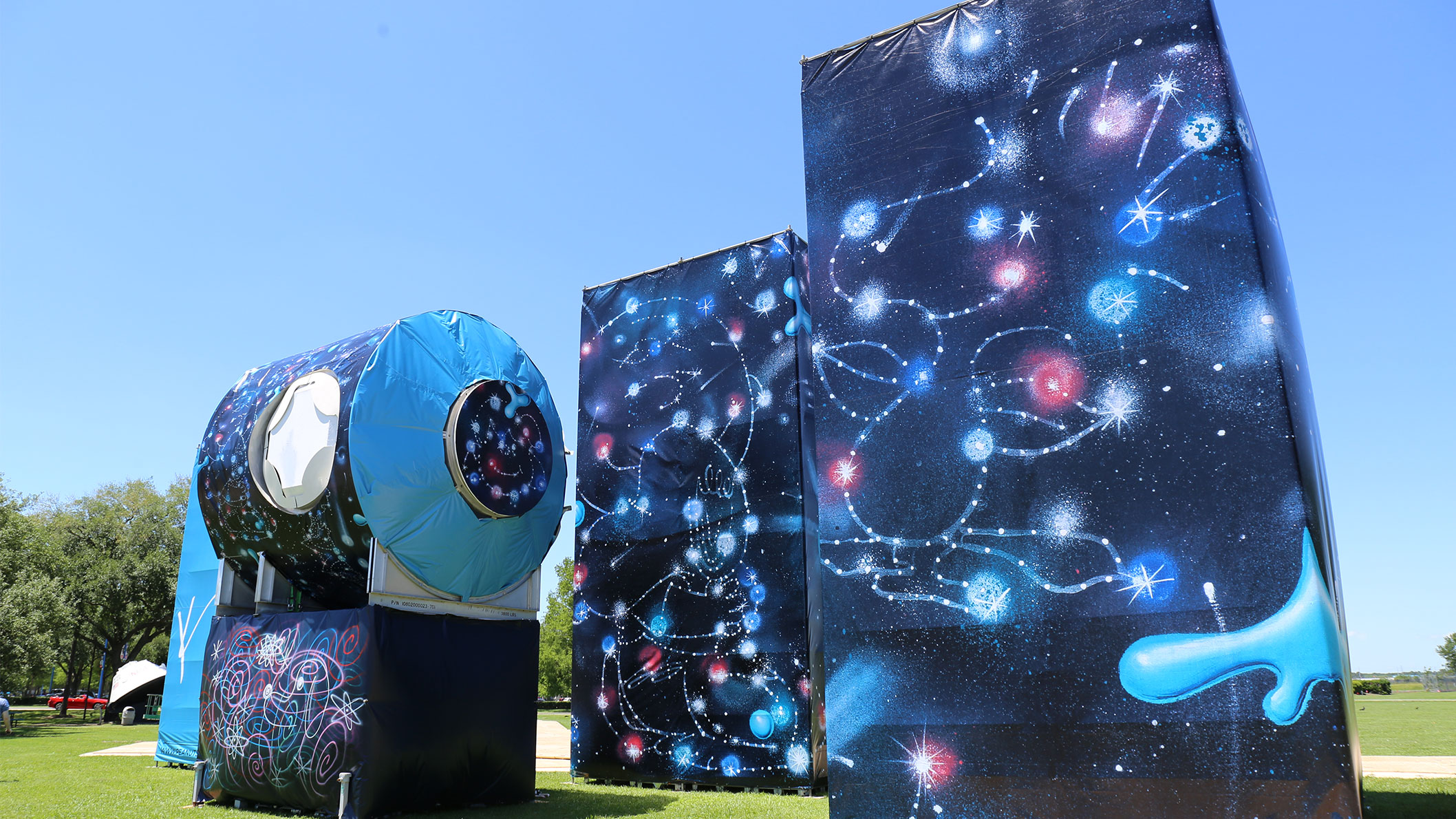 Three giant, spray-painted, blue structures in the middle of a green field.