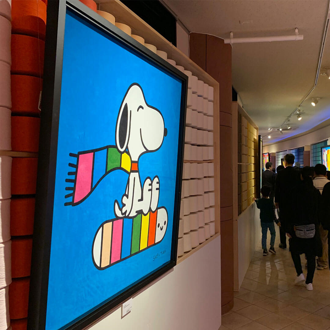 A TV hanging on a wall displaying a black and white dog wearing a colourful scarf. 