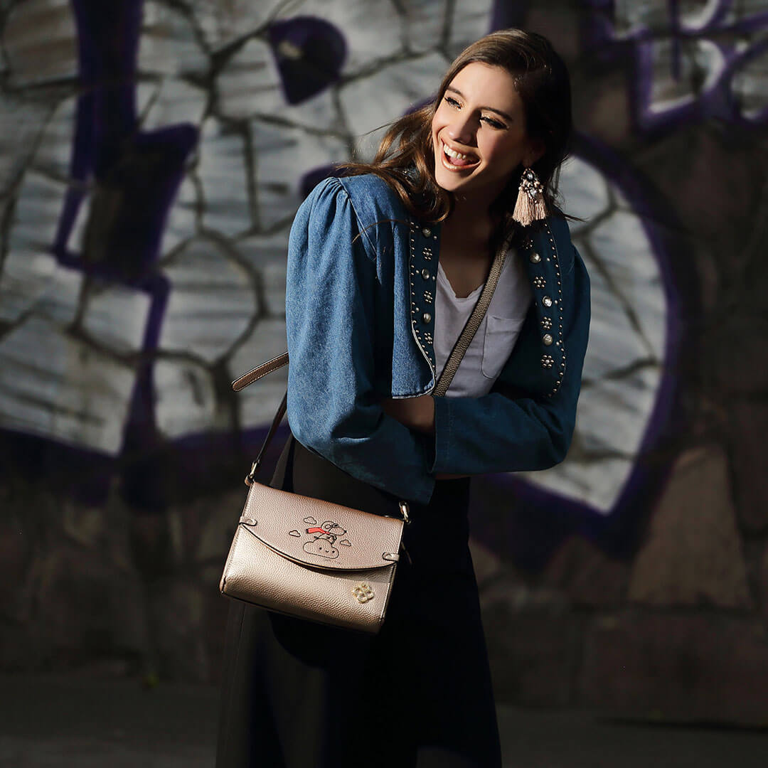 A brunette model walking in a graffiti alley, wearing a denim jacket, black skirt and a light pink purse.