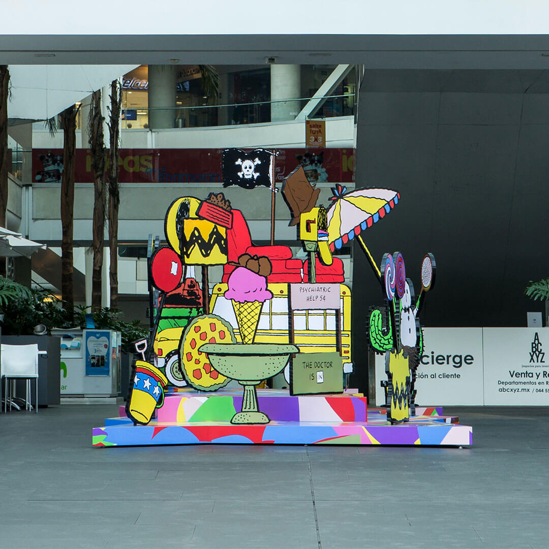 A colourful, 3D piece of art with many random objects including an icecream cone, a beach umbrella, and a school bus.