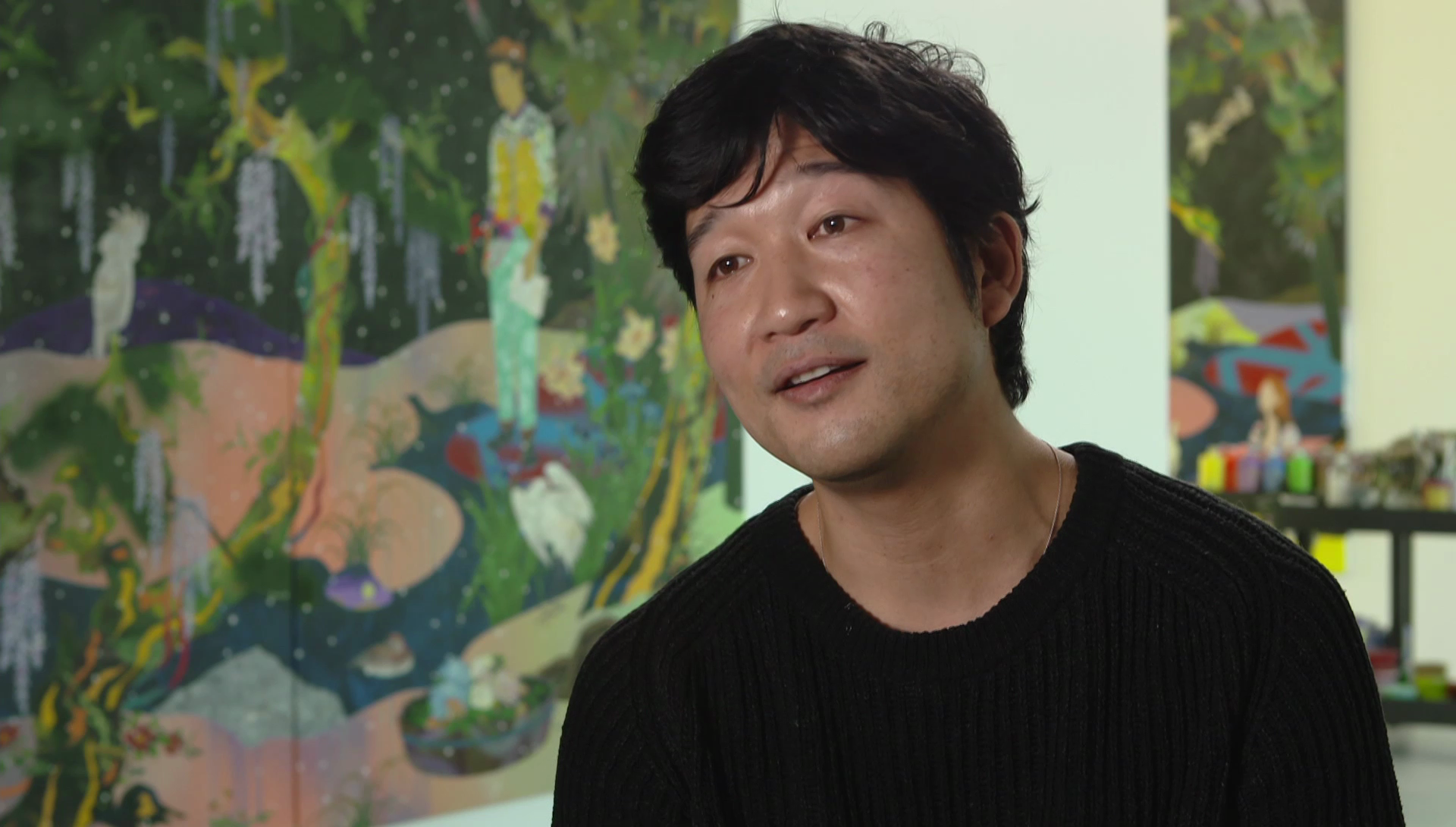 A close-up of a man talking with artwork in the background.