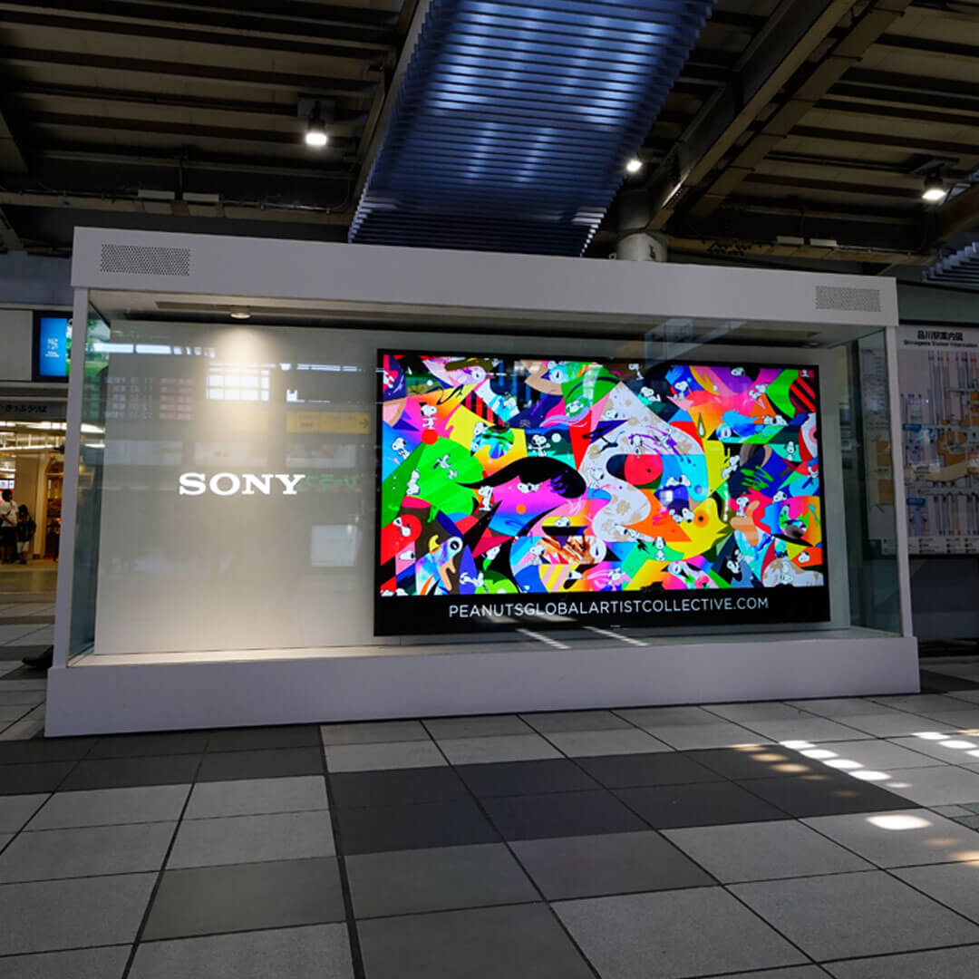 A bright LED display with a colourful image inside a train station.