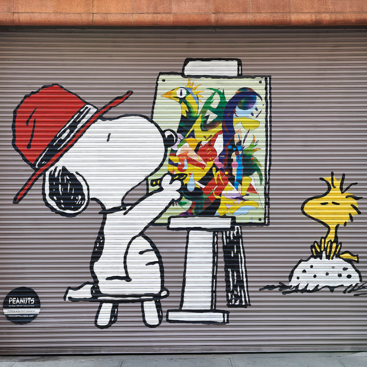 A black and white dog sitting on a chair, wearing a red hat and painting a picture. 