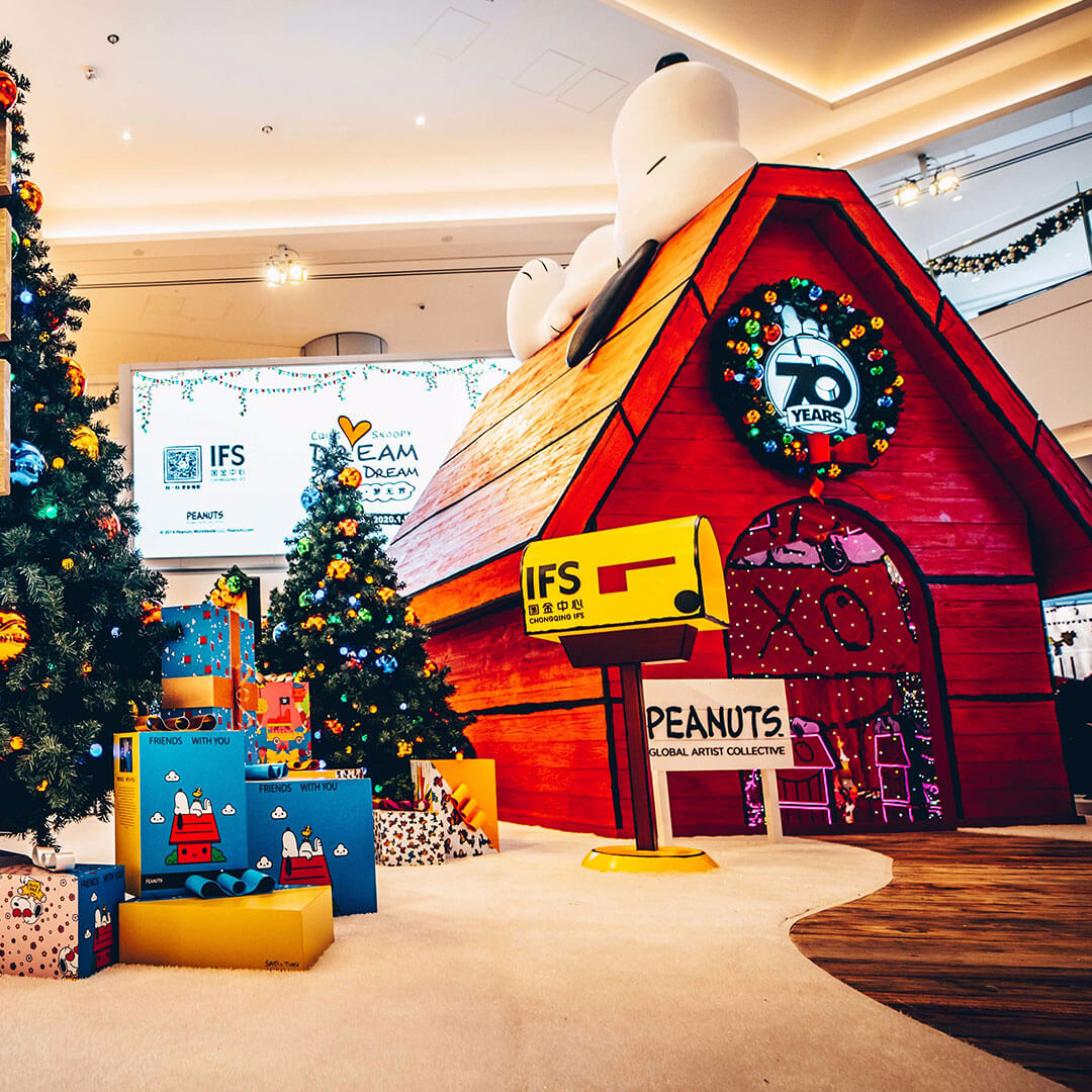 A large doghouse, a Christmas tree and presents inside a shopping mall.