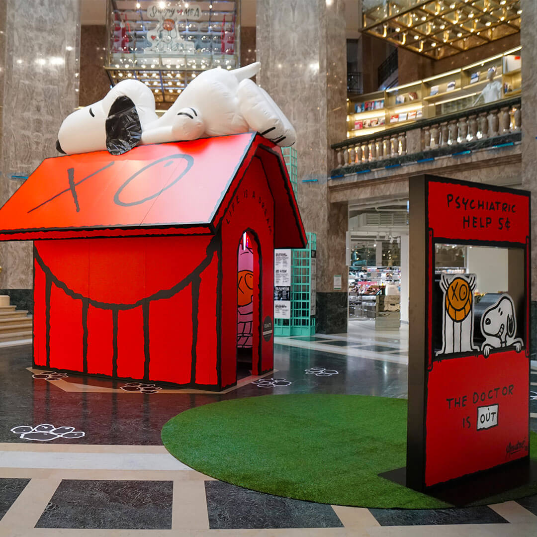 A display of red house with a black and white dog sleeping on the roof inside of a mall.